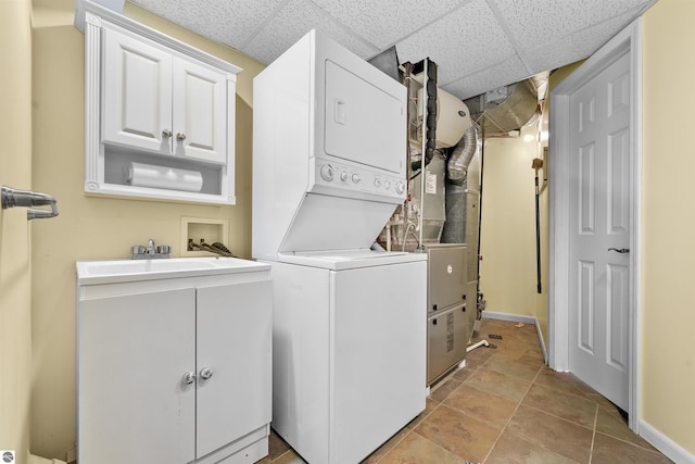 laundry area with cabinets, stacked washer and clothes dryer, and sink