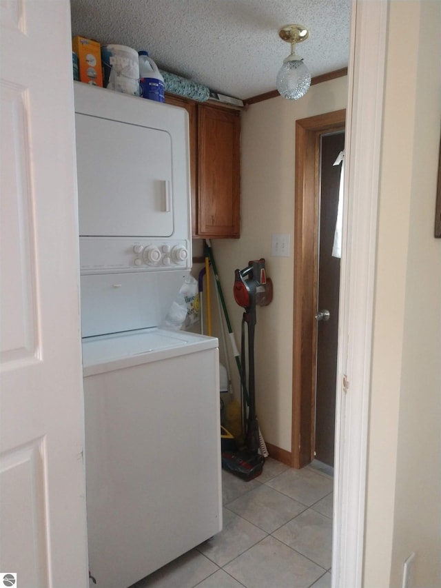 laundry area with stacked washer / dryer, light tile patterned flooring, cabinets, and a textured ceiling