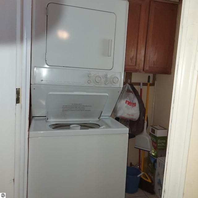 clothes washing area with cabinets and stacked washing maching and dryer