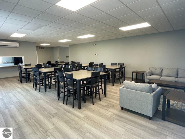 dining space featuring a drop ceiling, light hardwood / wood-style flooring, and a wall unit AC