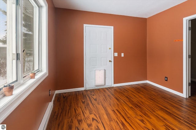 unfurnished room with dark hardwood / wood-style floors and a baseboard heating unit