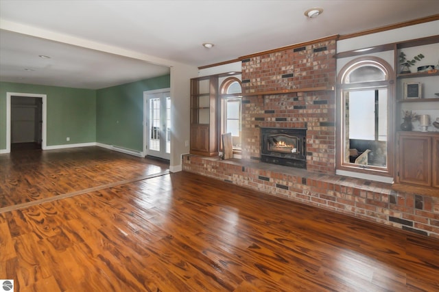 unfurnished living room featuring hardwood / wood-style flooring, baseboard heating, and a brick fireplace