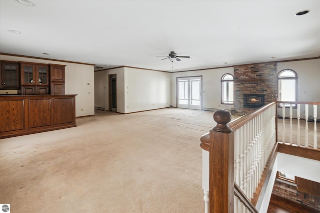 unfurnished living room with crown molding, ceiling fan, a fireplace, and light carpet