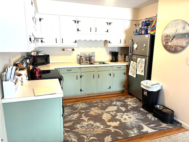 kitchen with white cabinetry, green cabinetry, stainless steel fridge, and sink