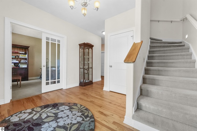 stairway featuring hardwood / wood-style flooring, a notable chandelier, and french doors