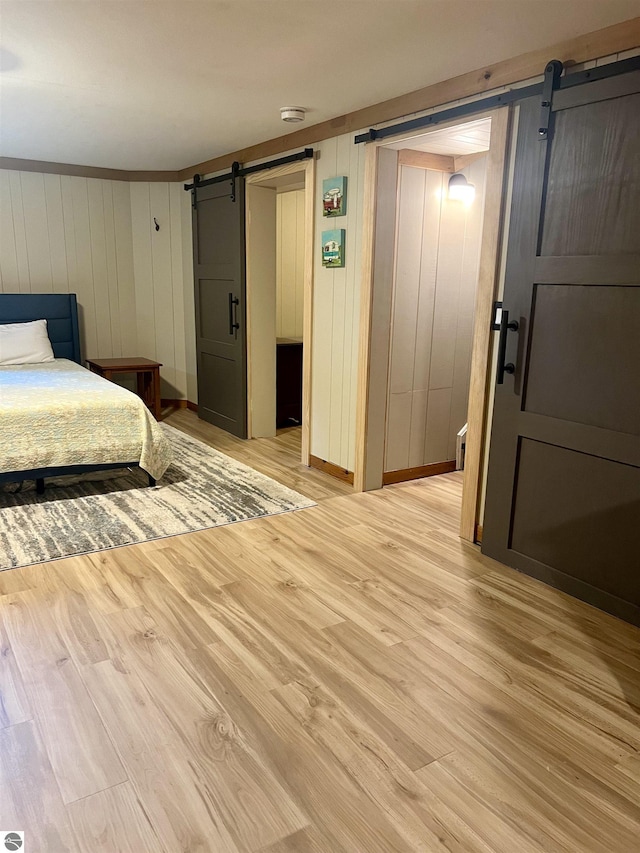 bedroom with a barn door and light wood-type flooring