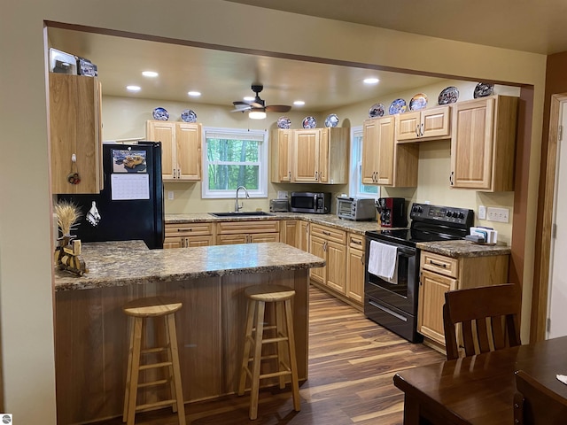 kitchen featuring a breakfast bar area, black appliances, and light brown cabinets