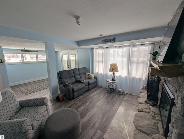 living room featuring hardwood / wood-style flooring, a stone fireplace, and a textured ceiling