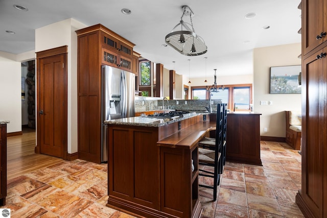 kitchen featuring a kitchen breakfast bar, a center island, stainless steel refrigerator with ice dispenser, decorative light fixtures, and dark stone counters