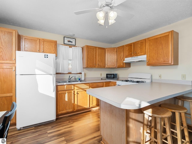 kitchen with sink, white appliances, a breakfast bar, light hardwood / wood-style floors, and kitchen peninsula