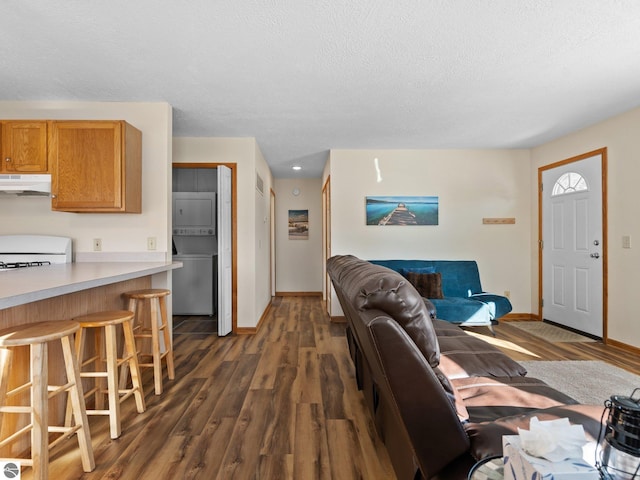 living room featuring dark hardwood / wood-style flooring, a textured ceiling, and stacked washing maching and dryer