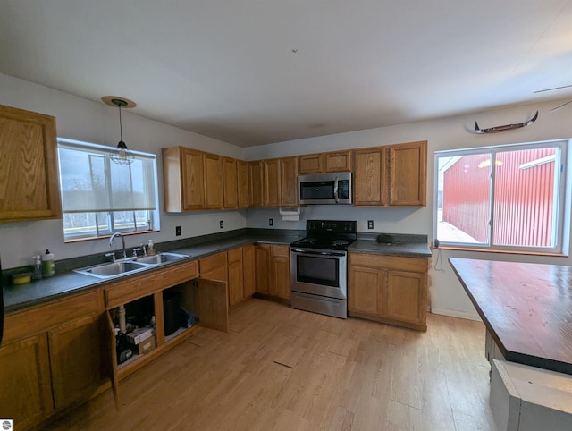 kitchen with appliances with stainless steel finishes, sink, pendant lighting, and light wood-type flooring