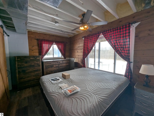 bedroom featuring ceiling fan, wood-type flooring, a barn door, and wood walls