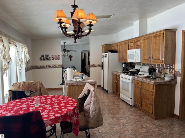 kitchen featuring an inviting chandelier, decorative light fixtures, a textured ceiling, dark tile patterned flooring, and white appliances