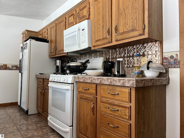 kitchen with tasteful backsplash, white appliances, tile counters, and dark tile patterned floors