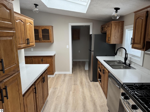 kitchen with sink, appliances with stainless steel finishes, lofted ceiling with skylight, light hardwood / wood-style floors, and a textured ceiling