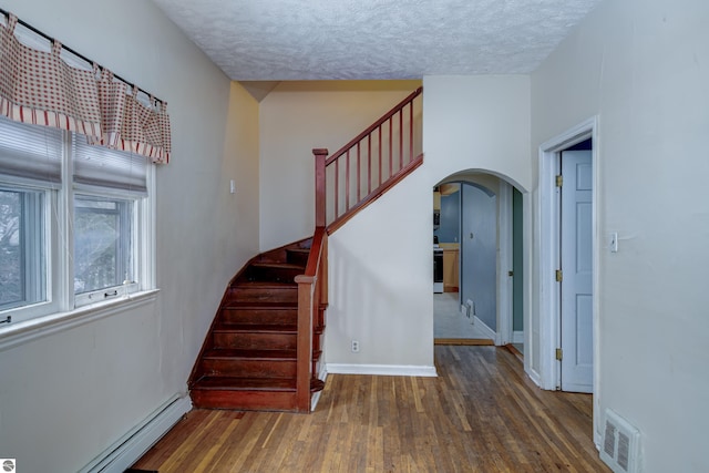 staircase featuring hardwood / wood-style floors, a textured ceiling, and baseboard heating