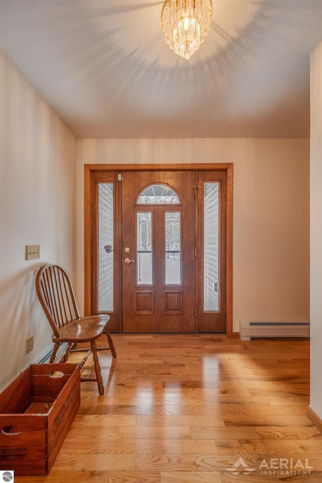 foyer entrance with light hardwood / wood-style flooring, a notable chandelier, a baseboard radiator, and a textured ceiling