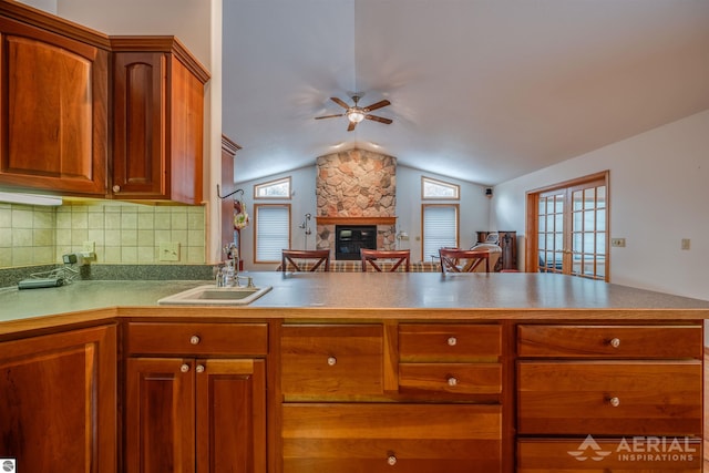 kitchen with a stone fireplace, sink, tasteful backsplash, vaulted ceiling, and kitchen peninsula