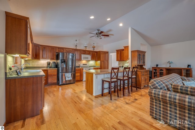 kitchen with sink, vaulted ceiling, light wood-type flooring, appliances with stainless steel finishes, and a kitchen breakfast bar