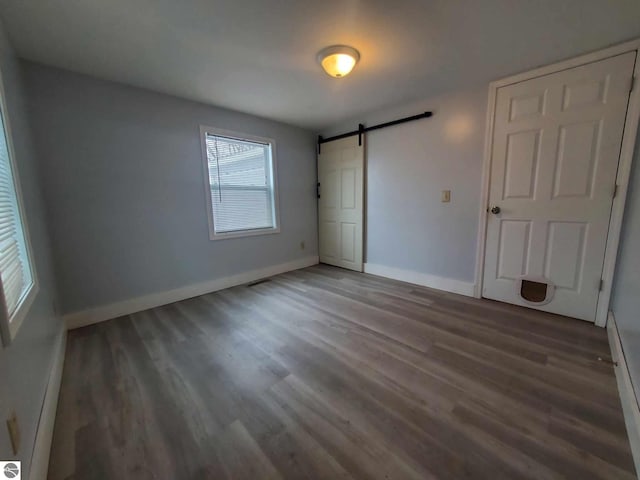 unfurnished bedroom with a barn door and dark hardwood / wood-style flooring