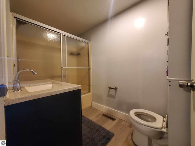 full bathroom with wood-type flooring, combined bath / shower with glass door, vanity, and toilet