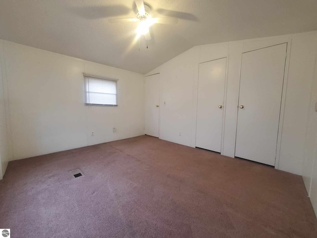 unfurnished bedroom featuring multiple closets, vaulted ceiling, carpet floors, and ceiling fan