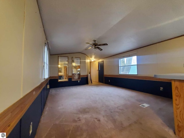 unfurnished living room with ceiling fan, lofted ceiling, and dark carpet