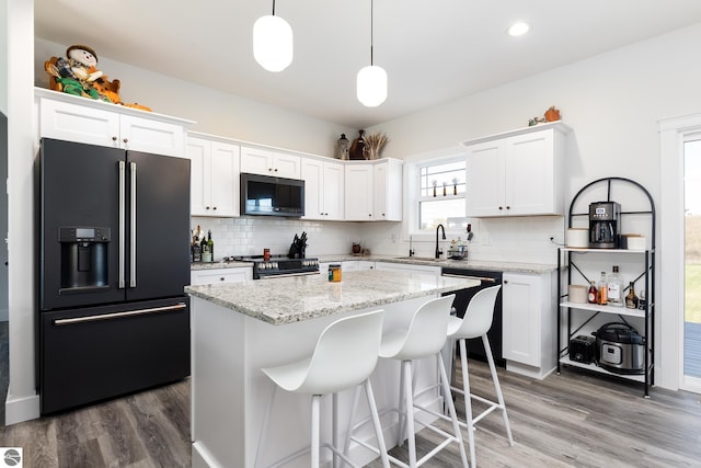 kitchen with pendant lighting, backsplash, black appliances, white cabinets, and a kitchen island