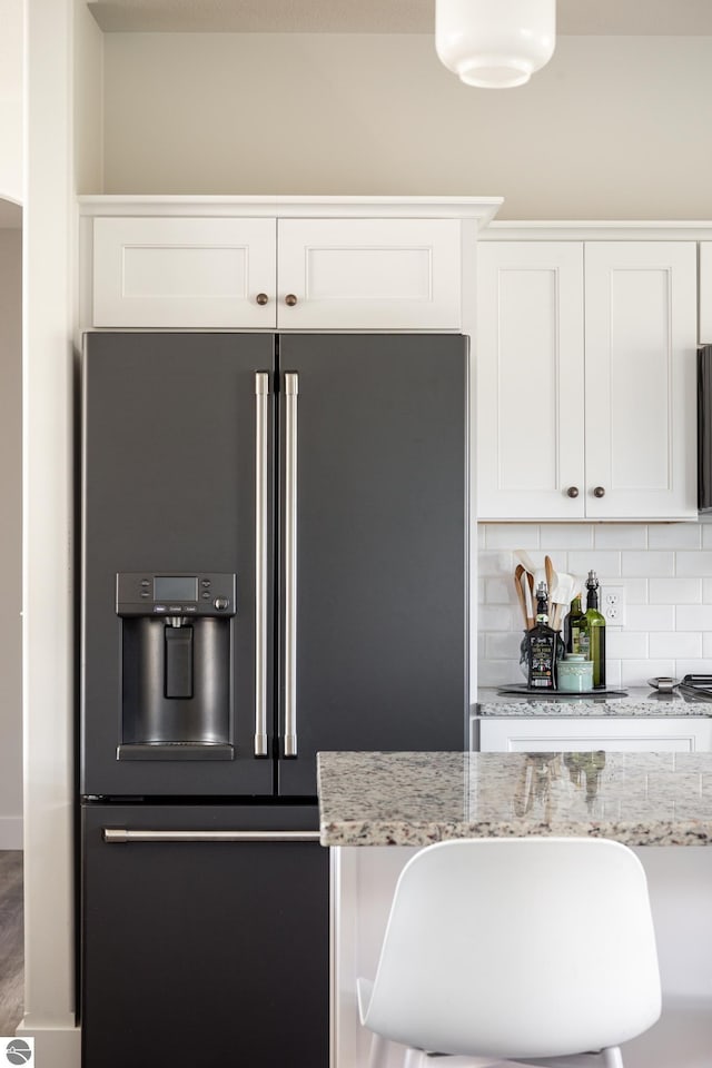 kitchen with a breakfast bar, high end fridge, light stone countertops, and white cabinets