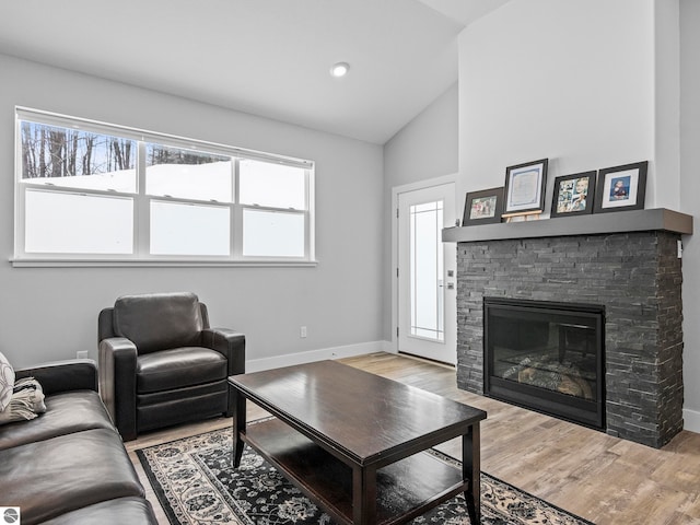 living room with lofted ceiling, a stone fireplace, plenty of natural light, and light wood-type flooring