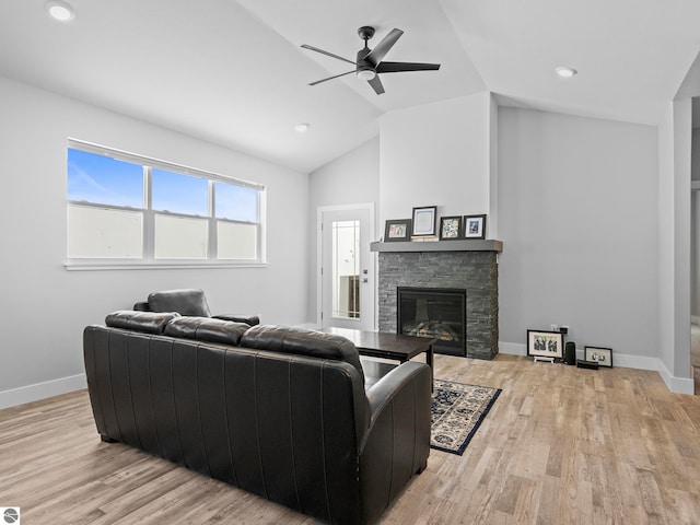 living room featuring ceiling fan, a stone fireplace, lofted ceiling, and light hardwood / wood-style floors