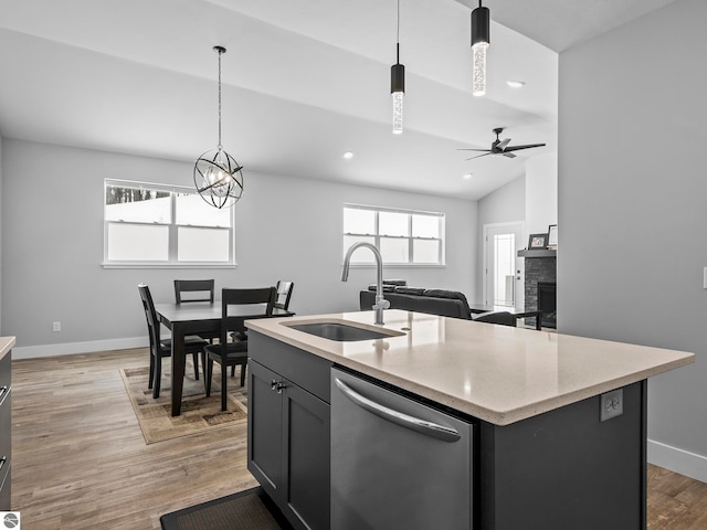 kitchen featuring a stone fireplace, sink, dishwasher, pendant lighting, and a kitchen island with sink