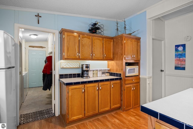 kitchen featuring crown molding, stainless steel refrigerator, light hardwood / wood-style floors, a textured ceiling, and tile countertops