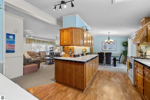 kitchen with ceiling fan with notable chandelier, decorative light fixtures, gas range gas stove, a textured ceiling, and light hardwood / wood-style flooring