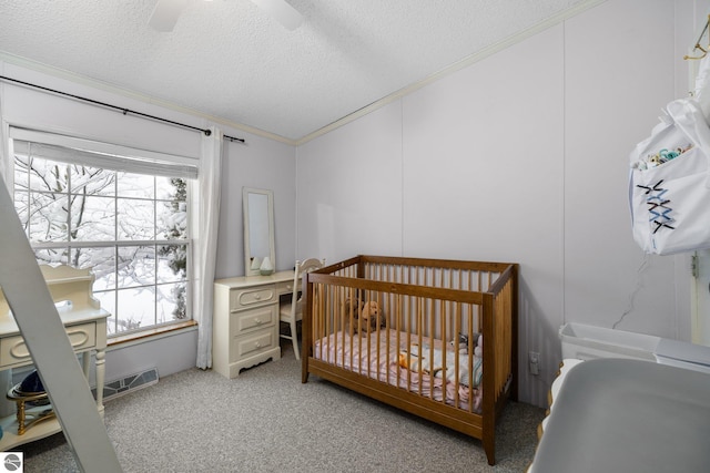 bedroom featuring a textured ceiling, ceiling fan, ornamental molding, a nursery area, and light colored carpet