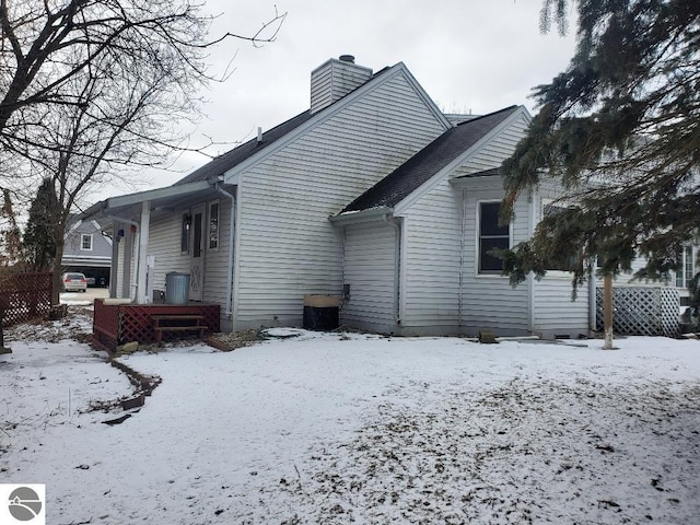 snow covered rear of property featuring a chimney