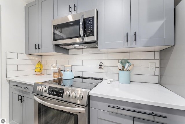 kitchen featuring gray cabinets, appliances with stainless steel finishes, backsplash, and light stone counters