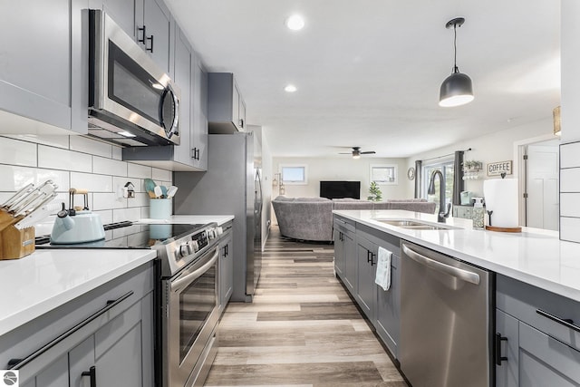 kitchen featuring sink, tasteful backsplash, appliances with stainless steel finishes, gray cabinets, and pendant lighting