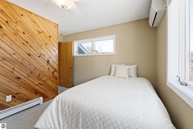 carpeted bedroom with a wall mounted air conditioner, a textured ceiling, wooden walls, ceiling fan, and a baseboard heating unit