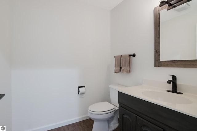 half bath featuring toilet, vanity, baseboards, and wood finished floors