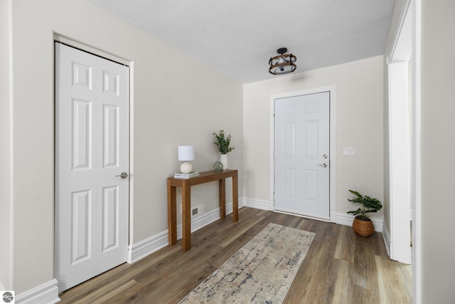 foyer entrance featuring visible vents, wood finished floors, baseboards, and a textured ceiling