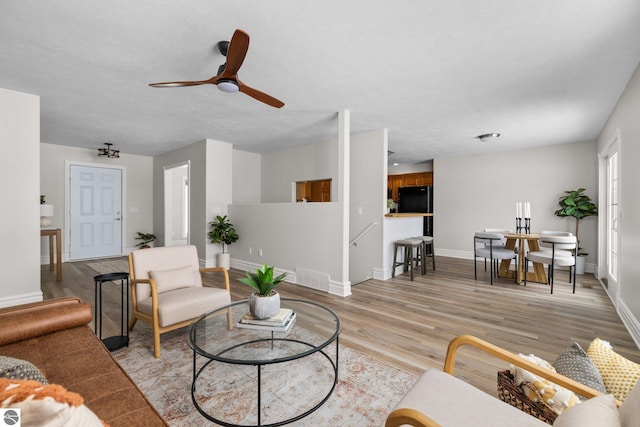 living area featuring light wood-type flooring, visible vents, baseboards, and ceiling fan