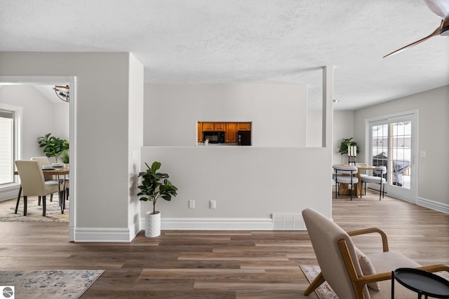 sitting room with a textured ceiling, wood finished floors, visible vents, and baseboards