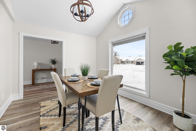 dining space with a chandelier, light wood finished floors, baseboards, and vaulted ceiling