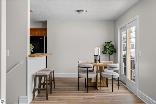 dining area featuring a textured ceiling, light wood-type flooring, and baseboards