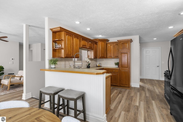 kitchen featuring a breakfast bar, a peninsula, freestanding refrigerator, wood finished floors, and open shelves