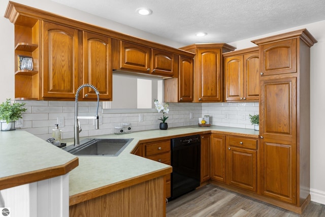 kitchen featuring backsplash, light wood-type flooring, light countertops, black dishwasher, and a sink