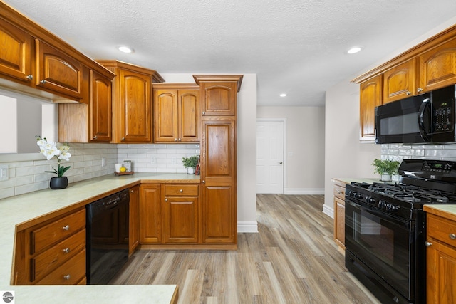 kitchen with brown cabinets, black appliances, light countertops, and light wood-style floors