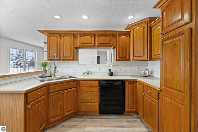 kitchen featuring a sink, a peninsula, light wood finished floors, dishwasher, and light countertops